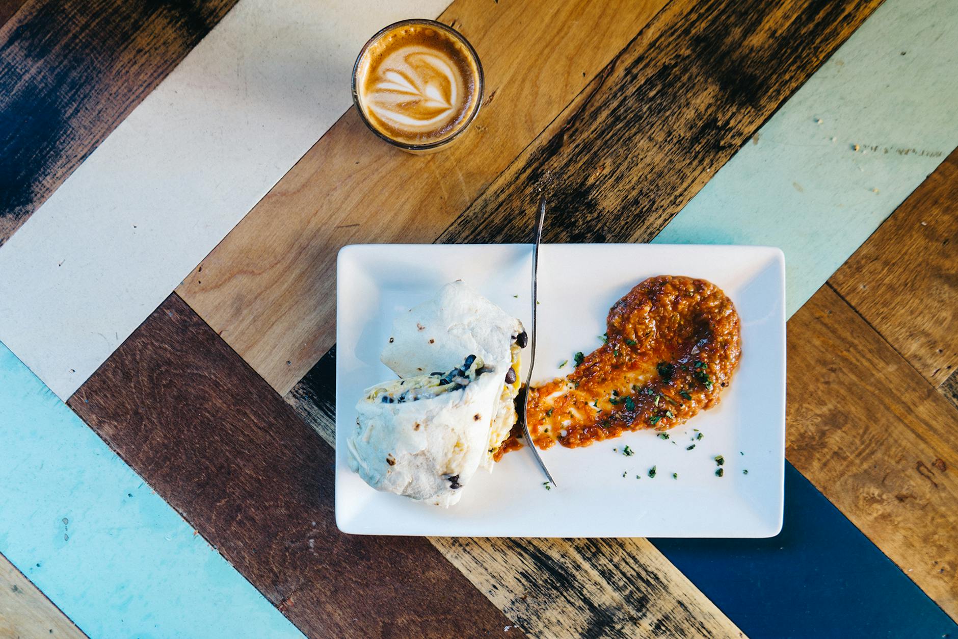 Śniadaniowe burrito z sosem i kawą na kolorowym drewnianym stole