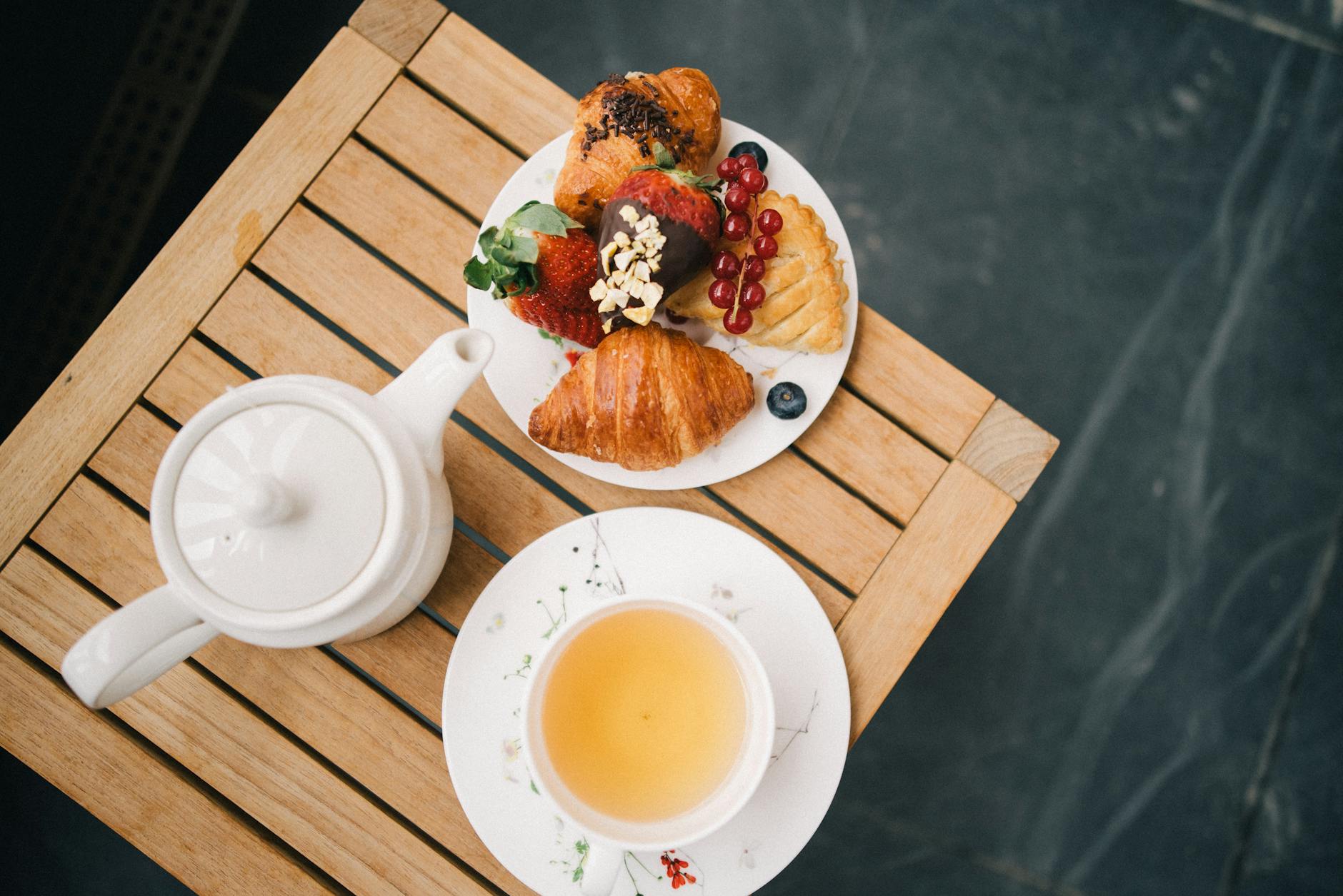 Śniadaniowy zestaw z herbatą, rogalikami i owocami na drewnianym stole