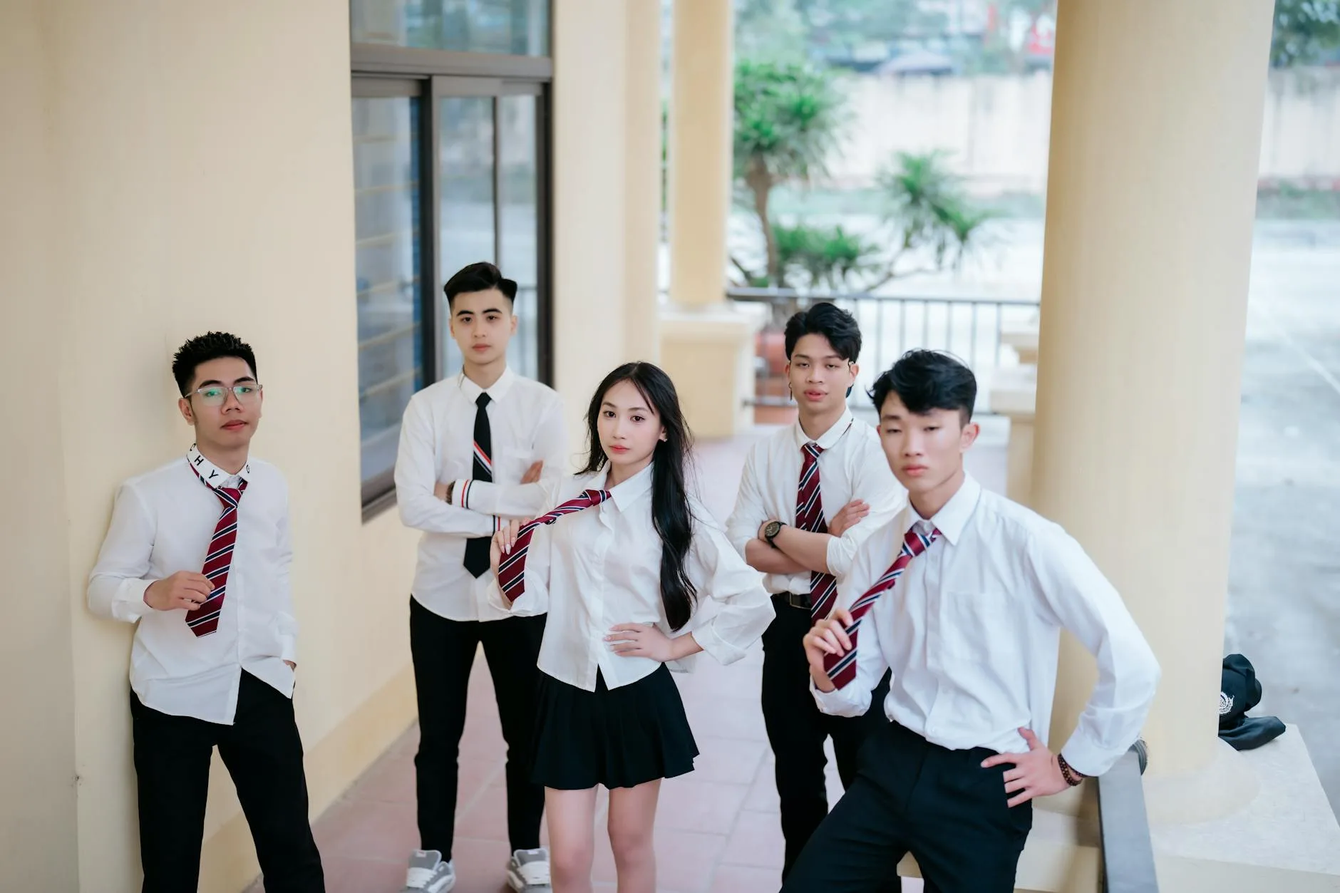 Uczniowie w szkolnych mundurkach stoją przed budynkiem szkoły