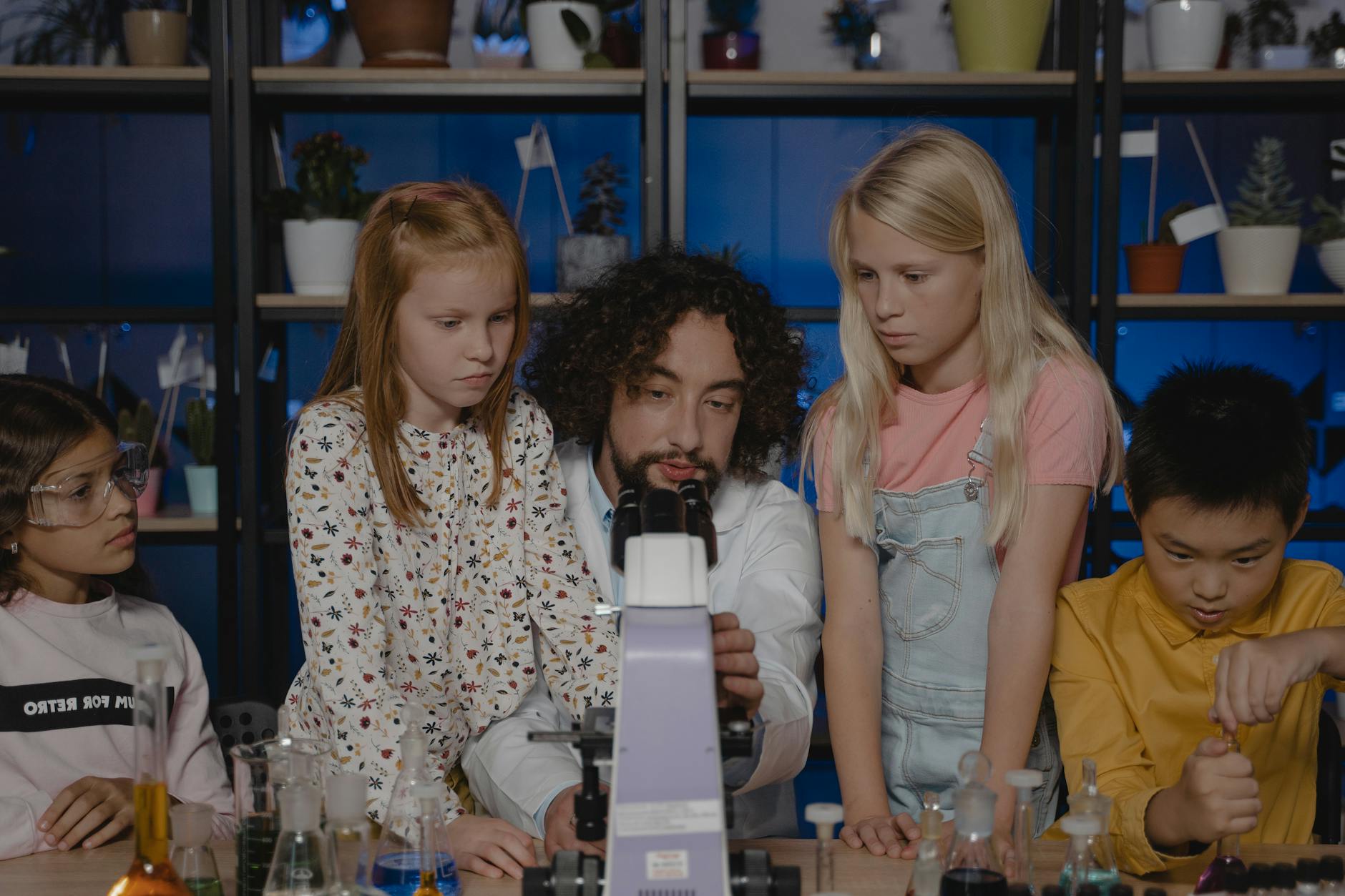 Nauczyciel i uczniowie obserwują preparat pod szkolnym mikroskopem