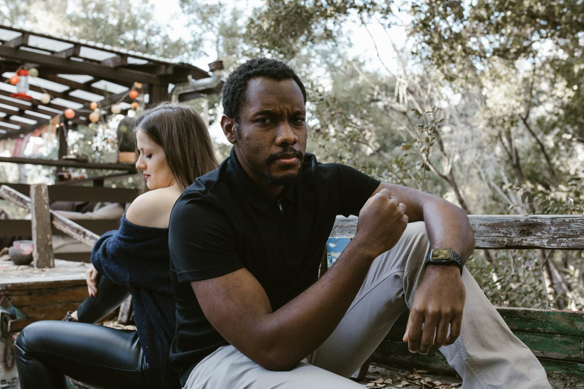 Zamyślony mężczyzna siedzi na dworze, za nim kobieta w oddaleniu