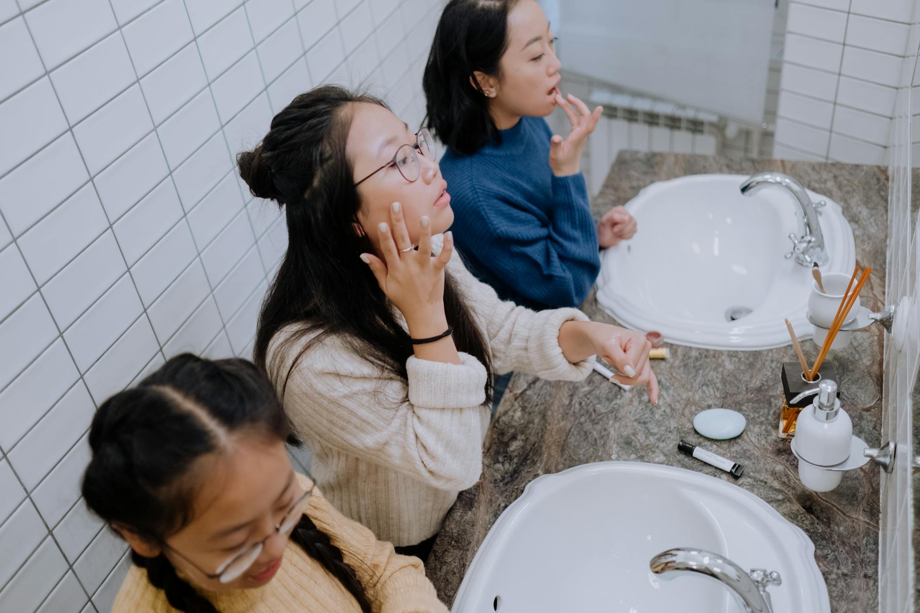 Trzy nastolatki nakładają kosmetyki w łazience, dbając o wygląd