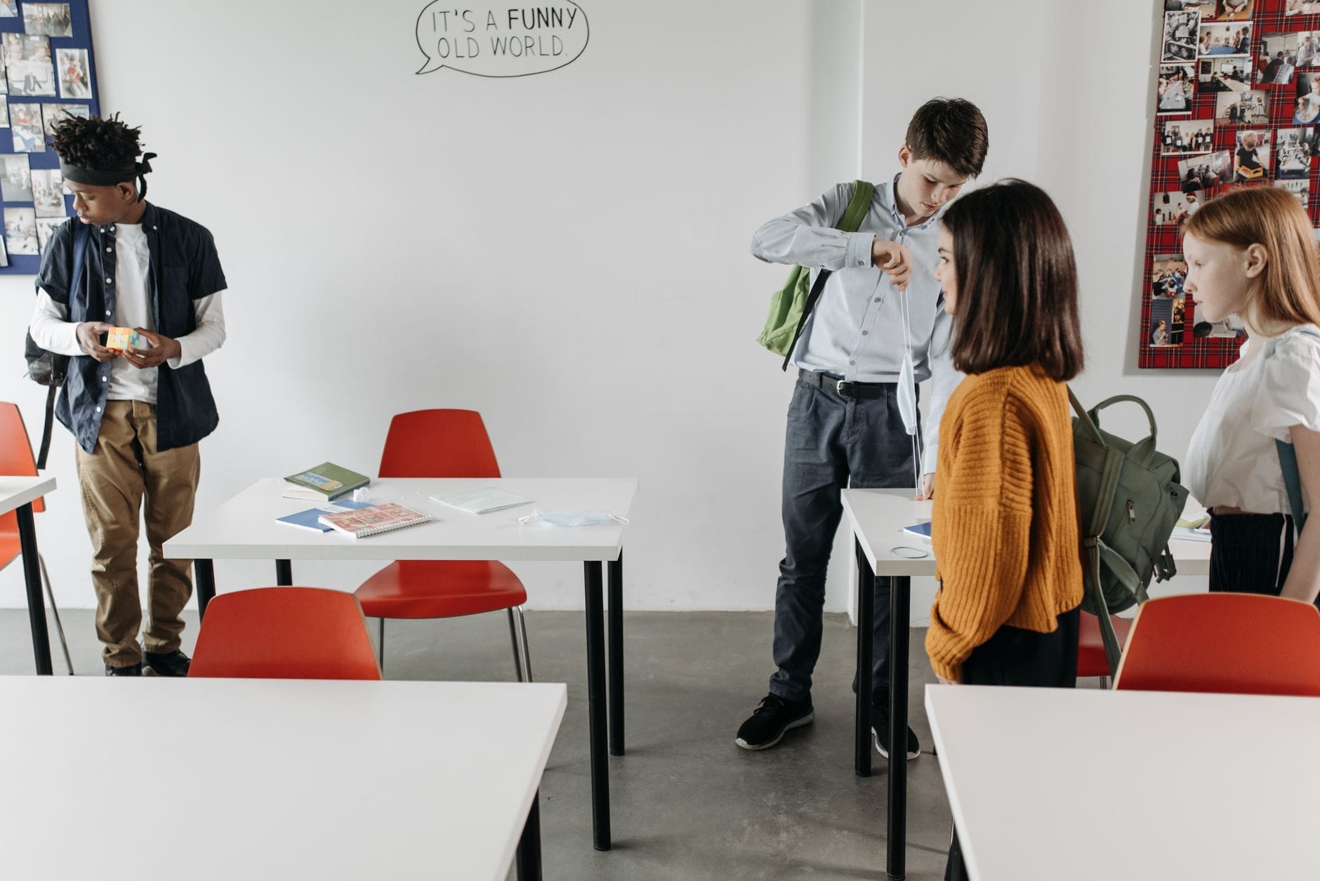 Uczniowie rozmawiają w klasie przy białych ławkach i czerwonych krzesłach